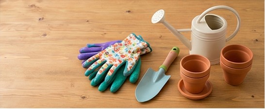 木製のテーブルの上にきれいに並べられた、スコップ、ジョウロ、剪定ばさみ、園芸用手袋などの基本的な園芸道具一式。