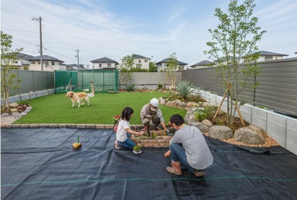 雑草対策のために、庭の土の上に耐久性の高い黒色の防草シートを丁寧に施工しているプロの作業風景