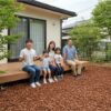 ウッドチップが敷き詰められた自然豊かな庭のウッドデッキで、笑顔でくつろぐ日本人の家族
